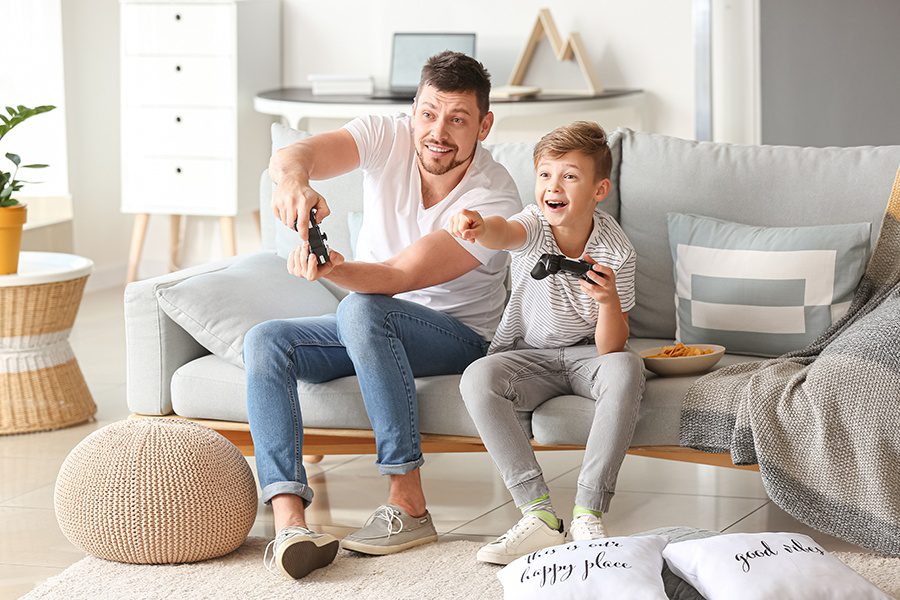 Personal Insurance - Father and Son Playing Video Games at Home on the Sofa